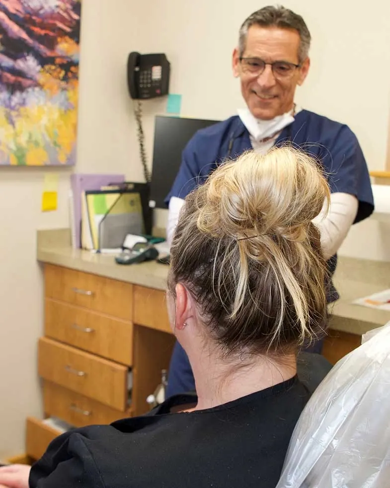 A dentist talking with a patient in a treatment room at 1330 Dental Associates.